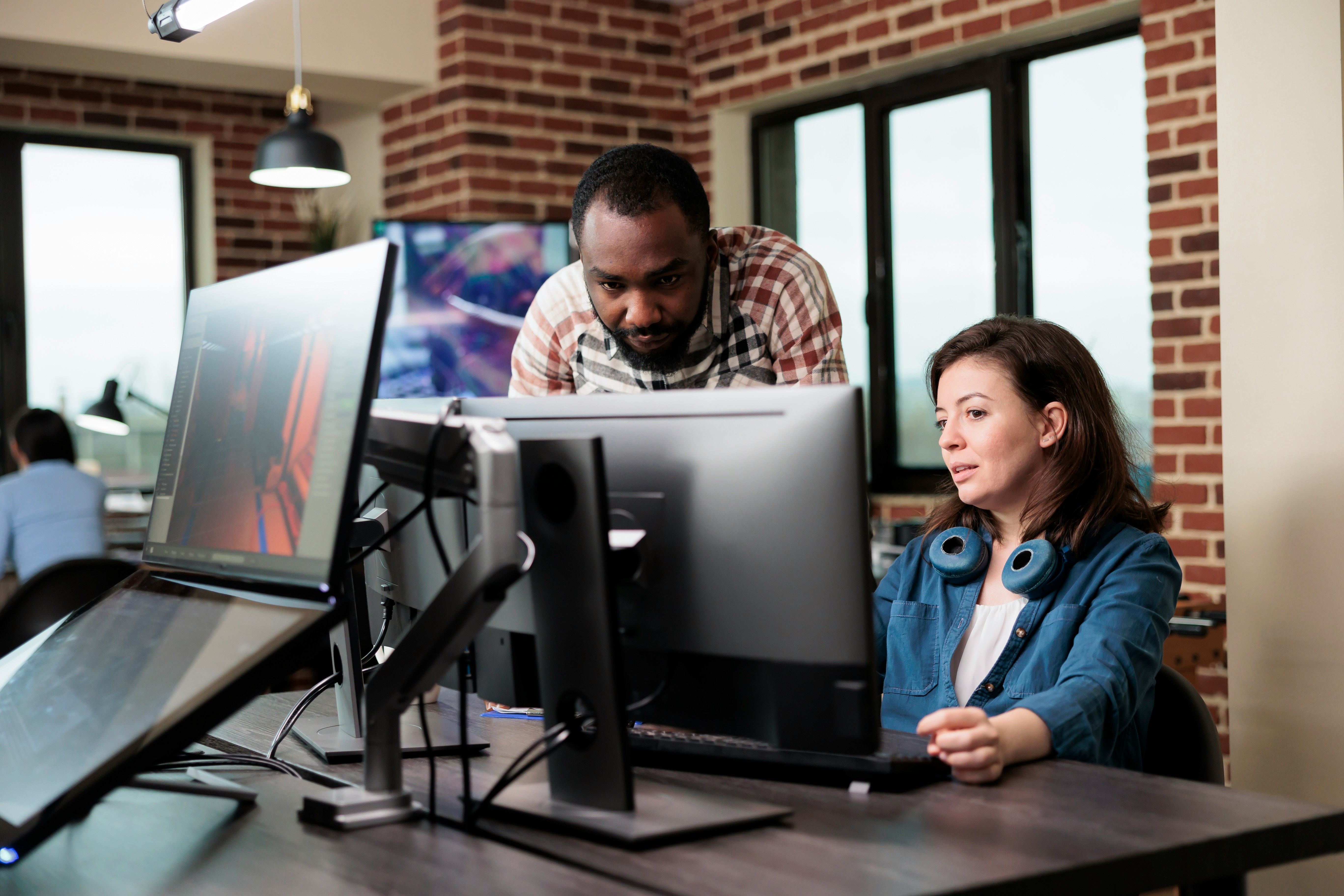 Man and woman looking at a computer screen at a desk. The woman is sitting and the man is standing leaning over
